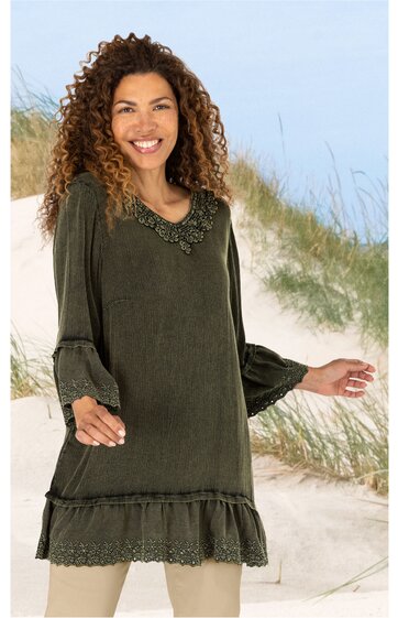 Dunkelolivgrünes Kleid mit Rundhals Ausschnitt, Spitzenbesatz am Kragen und Saum, lange Ärmel mit Volant und Spitzenabschluss, locker sitzend, getragen von stehender lächelnder Frau vor sandiger Dünenlandschaft