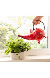 Gießkanne in Form eines roten Elefanten mit bunten Blumenmustern, langem Rüssel, schwarzen Griff, gehalten von Hand über grünem topfpflanze in grauem Blumentopf auf Fensterbank