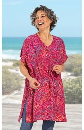 Rotes langes Sommerkleid mit floralem Muster, V-Ausschnitt, kurze Fledermausärmel, seitliche Schlitze, locker sitzend, getragen von lächelnder Frau vor Strandkulisse