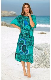 Midikleid in türkis mit abstraktem blau-schwarzem Muster, rundhalsausschnitt, kurze weite Ärmel, lockere Passform, getragen von barfuß stehender Frau am Strand