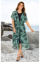 Schwarzes Midikleid, darüber leichtes Überwurfkleid in Dunkelgrün mit Hellgrünen Blattmustern, kurze Ärmel, offene Front, Taillenzug, getragen von stehender lächelnder Frau am Strand