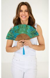 Handfächer mit grünem und blauem Muster, brauner Griff mit hellblauem Quastenanhänger, gehalten von lächelnder Person in weißem ärmellosem Oberteil und weißer Hose, Fächer vor Gesicht