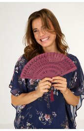 Fächer in Dunkelrosa mit gemusterten Aussparungen, längliche Form, gehalten von lächelnder Frau in dunklem, blumigem Oberteil mit transparenten Ärmeln