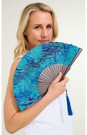 Handfächer in Türkis mit dunkelblauem floralem Muster, grauer Fächergriff mit blauer Quaste, gehalten von stehender Frau in weißem ärmellosem Oberteil