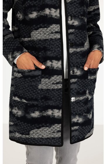 Langer Mantel mit Taschen, schwarz und dunkelgrau gemustert in Streifenoptik, gerade geschnitten, Knopfleiste, getragen von stehender Person mit Händen in den Taschen