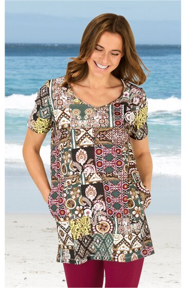 Kurzärmliges Tunika-Shirt in gemusterten Braun-, Grün- und Beigetönen, gemischtes geometrisches und florales Muster, Rundhals, lockere Passform, getragen von lächelnder Frau am Strand stehend, mit Taschen