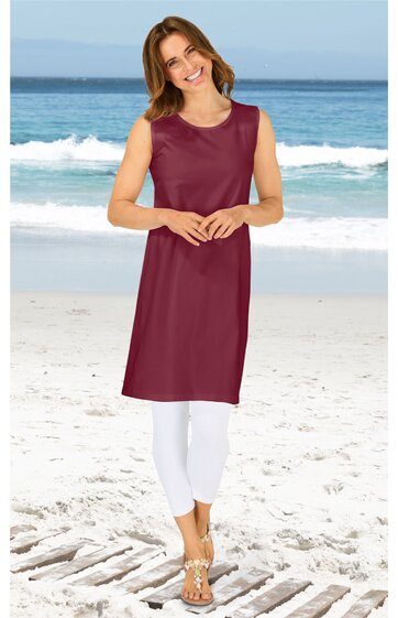 Ärmelloses, knielanges Kleid in dunkelrot, ohne Muster, rundhalsausschnitt, gerade geschnitten, getragen von lächelnder stehender Frau am Strand, kombiniert mit weißen Leggings und Sandalen