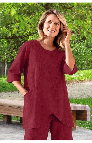 Weinrotes Oberteil mit lockerem Schnitt, asymmetrischem Saum, 3/4-Ärmeln, Rundhals, zwei seitlichen Eingrifftaschen, getragen von stehender Frau mit lockerem Haar