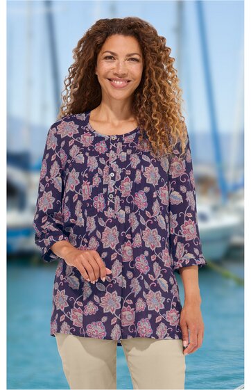 Dunkelblaues Damenoberteil mit hellrosa Blumenmuster, rundem Ausschnitt, lange Ärmel, lockere Passform, getragen von stehender Frau vor unscharfem Hintergrund mit Segelbooten