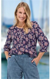 Bluse mit floralen Muster in Altrosa und Hellgrau auf dunkelblauem Grund, V-Ausschnitt mit kleiner Knopfleiste, lange Ärmel mit Bündchen, getragen von stehender Frau mit Händen in Hosentaschen