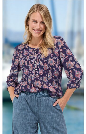 Bluse mit floralen Muster in Altrosa und Hellgrau auf dunkelblauem Grund, V-Ausschnitt mit kleiner Knopfleiste, lange Ärmel mit Bündchen, getragen von stehender Frau mit Händen in Hosentaschen