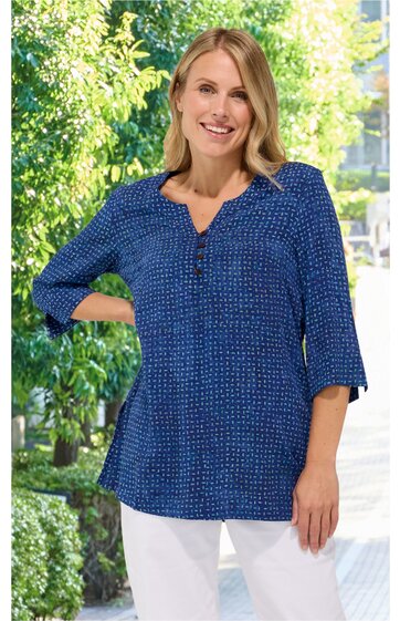 Dunkelblaue Bluse mit kleinen weißen Punkten, V-Ausschnitt mit Knopfleiste, 3/4-lange Ärmel, gerade Form, getragen von stehender lächelnder Frau vor grünem Hintergrund