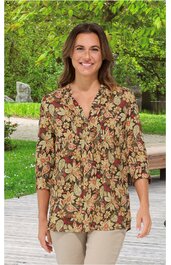 Locker geschnittene Bluse in Braun mit floralen Mustern in Gelb und Rot, V-Ausschnitt, lange Ärmel mit Bündchen, getragen von stehender Frau vor grünem Hintergrund