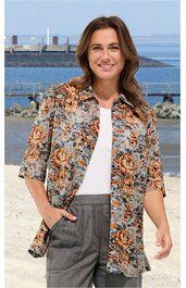 Bluse mit floralem Muster in Orange, Hellblau, Grau und Schwarz, mit durchgehender Knopfleiste, halblangen Ärmeln, umgelegtem Kragen, lockerer Schnitt, getragen von lächelnder Frau am Meer