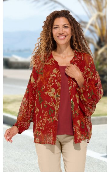 Rotes, locker geschnittenes Damenoberteil mit floralem Muster, langer weiter Ärmel, offener Schnitt, getragen von lächelnder, stehender Frau, darunter rotes Rundhalstop, beige Hose