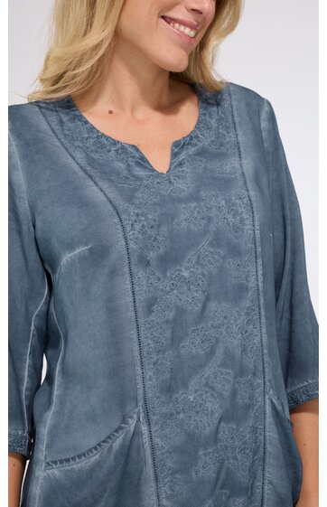 Graues Oberteil mit floralem Muster, V-förmiger Ausschnitt, 3/4-Ärmel, rundem Kragen, aufgesetzte Taschen, getragen von lächelnder stehender Frau