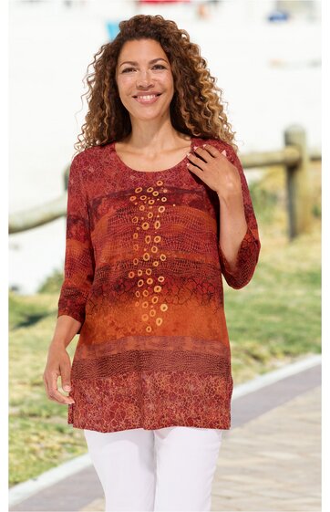 Rostrotes Langarmshirt mit verschiedenfarbigen Mustern, Rundhalsausschnitt, mittellang, mit bronzefarbenen Ösen in vertikaler Anordnung vorne, getragen von stehendem, lächelndem Model, weiße Hose