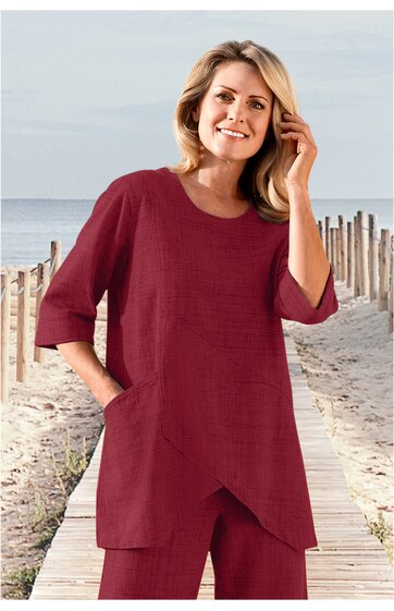 Weinrotes langärmeliges Oberteil mit asymmetrischem Saum, rundem Ausschnitt, locker geschnitten, getragen von lächelnder stehender Frau am Strand