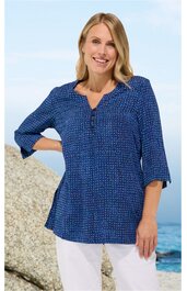 Damenbluse in Dunkelblau mit kleinen weißen Punkten, V-Ausschnitt mit Knopfleiste, 3/4-Ärmel, locker sitzend, getragen von lächelnder Frau stehend vor Felsen und Meer