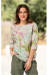 Bluse in hellem Pastellgrün mit floralem Muster in Rosatönen und zarten Grüntönen, rundhalsausschnitt, dreiviertellange Ärmel, lockere Passform, getragen von stehender Frau mit Händen in Taschen