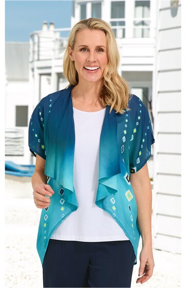 Blauer Cardigan mit Farbverlauf von Dunkel- zu Hellblau, geometrisches Muster in Weiß und Gelb, kurze Fledermausärmel, offene Front mit locker fallenden Volants, getragen von lächelnder Frau in stehender Position