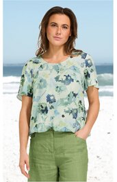 Bluse in hellem Mintgrün mit blauem Blumenmuster, Rundhalsausschnitt, kurze Ärmel, lockere Passform, getragen von woman vor Strandozean im Hintergrund