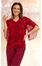 Rotes Damenoberteil mit abstraktem Muster, V-Ausschnitt, weite kurze Ärmel mit transparenten Einsätzen, tailliert, getragen von lächelnder Frau mit hochgezogenem Arm und Glas in der Hand