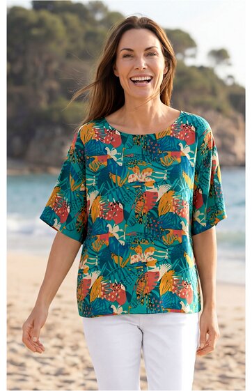 Türkisgrüner Damenpullover mit buntem Blumen- und Blättermuster, runder Ausschnitt, halblange Ärmel, locker geschnitten, getragen von lächelnder Frau mit offenen Haaren am Strand