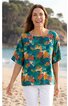 Türkisgrüner Damenpullover mit buntem Blumen- und Blättermuster, runder Ausschnitt, halblange Ärmel, locker geschnitten, getragen von lächelnder Frau mit offenen Haaren am Strand