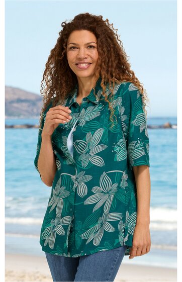 Grüne Bluse mit großen weißen Blütenmustern, Hemdblusenkragen, halblange Ärmel, längs geschnitten, getragen von lächelnder Frau stehend am Strand