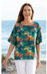 Blusenshirt türkis mit großem floralen Blatt- und Blumenmuster in Orange, Rot und Hellgrün, kurze, weite Ärmel, runder Ausschnitt, gerade geschnitten, getragen von stehender Frau vor Meereskulisse