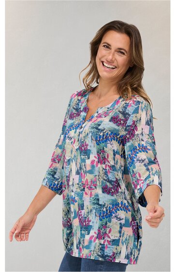 Lange Bluse in hellgrau mit abstraktem Muster in Pink, Blau und Türkis, halblange Ärmel mit Bündchen, V-Ausschnitt mit Schlitz und Knopfleiste, locker geschnitten, getragen von lächelnder Frau in stehender Pose