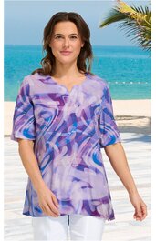 Lila bunt gemustertes T-Shirt mit abstraktem Muster, V-Ausschnitt, halblange Ärmel, gerade geschnitten, getragen von stehender Frau vor Meereskulisse