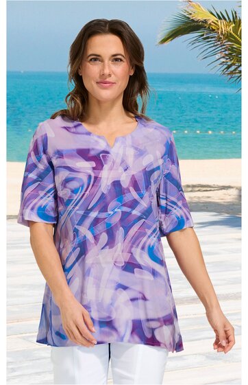Lila bunt gemustertes T-Shirt mit abstraktem Muster, V-Ausschnitt, halblange Ärmel, gerade geschnitten, getragen von stehender Frau vor Meereskulisse