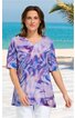 Lila bunt gemustertes T-Shirt mit abstraktem Muster, V-Ausschnitt, halblange Ärmel, gerade geschnitten, getragen von stehender Frau vor Meereskulisse