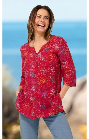 Rote Bluse mit buntem kreisförmigem Muster, V-Ausschnitt, 3/4-Arm, lockere Passform, getragen von stehender Frau mit lächelndem Gesichtsausdruck, Seitentaschen, legere Länge bis zur Hüfte