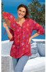 Rotes Blusenshirt mit runden weißen und orangefarbenen Mustern, V-Ausschnitt mit Knopfleiste, dreiviertellange Ärmel, locker geschnitten, getragen von lächelnder stehender Frau mit Fächer in der rechten Hand vor Außenbereich mit Korbmöbeln und Pflanz