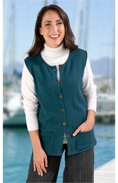 Ärmellose Weste in dunklem Petrol, durchgehende Knopfreihe mit braunen Knöpfen, zwei aufgesetzte Taschen vorne, rundem Halsausschnitt, getragen von lächelnder Frau mit weißen langärmligem Rollkragenpullover und dunkler Hose, gerade geschnitten