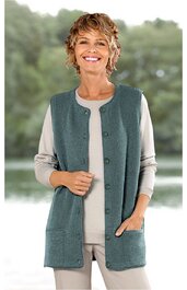 Ärmellose Strickweste in graugrün, ohne Muster, vorne mit Knöpfen, zwei aufgesetzte Taschen, gerade geschnitten, getragen von lächelnder Frau in hellbeiger langärmliger Bluse und Hose, stehend