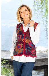 Ärmellose Strickweste in Dunkelrot mit großflächigem Blumenmuster in Blau, Orange und Violett, V-Ausschnitt, Knopfleiste vorne, getragen von stehender Frau mit weißer Bluse und blauer Hose