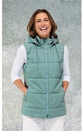 Hellgrüne gesteppte Damenweste mit Stehkragen und Kapuze, durchgehender Reißverschluss, Ärmellos, zwei seitliche Eingrifftaschen, getragen von lächelnder Frau mit weißen Dreiviertelarmshirt und weißer Hose