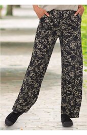 Schwarze Hose mit beigem floralen Muster, weite Beine, elastischer Bund, zwei Taschen, getragen von stehender Person mit Händen in den Taschen