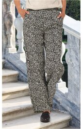 Locker sitzende schwarze Hose mit weißem abstraktem Linienmuster, gerade geschnitten, Seitentaschen, getragen von stehender Person mit Händen in den Taschen