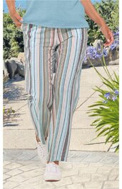 Weiß-bunte, gestreifte lange Hose mit geradem Bein, getragen von stehender Person, kombiniert mit hellblauem Oberteil und weißen Sportschuhen