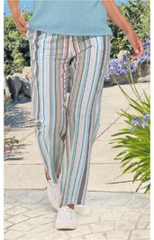 Weiß-bunte, gestreifte lange Hose mit geradem Bein, getragen von stehender Person, kombiniert mit hellblauem Oberteil und weißen Sportschuhen