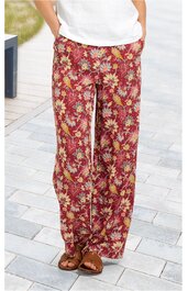 Weite Hose in rostrot mit gelbem und beige floralem Muster, elastischer Bund, zwei Eingrifftaschen, getragen von stehendem Modell mit weißen Schuhen und weißem Oberteil