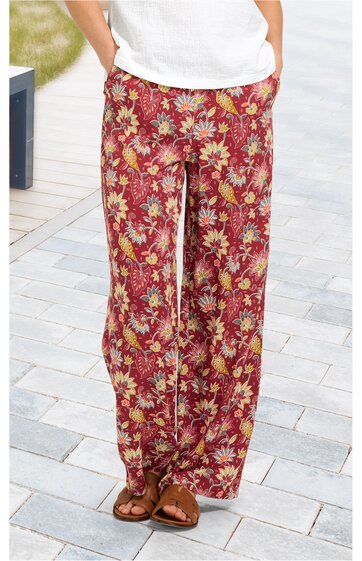 Weite Hose in rostrot mit gelbem und beige floralem Muster, elastischer Bund, zwei Eingrifftaschen, getragen von stehendem Modell mit weißen Schuhen und weißem Oberteil
