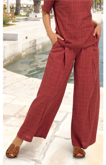 Rostbraunes zweiteiliges Outfit mit feinem Karomuster, kurzärmeliges Oberteil mit Rundhalsausschnitt, weite lange Hose, getragen von stehender Person, helle Sandalen, Hände in den Hosentaschen