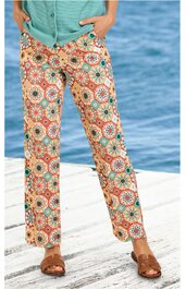 Hose mit weitem Bein, hellbeige Grundfarbe, buntes geometrisches Muster mit orange, blau und grün, gerade geschnitten, getragen von stehender Person, kombiniert mit türkisfarbenem Oberteil und braunen Sandalen