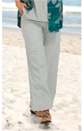 Hellgraue lange Hose mit geradem Bein, ohne sichtbare Taschen, getragen von stehender Person am Strand, kombiniert mit sandfarbenen Sandalen mit Verzierung